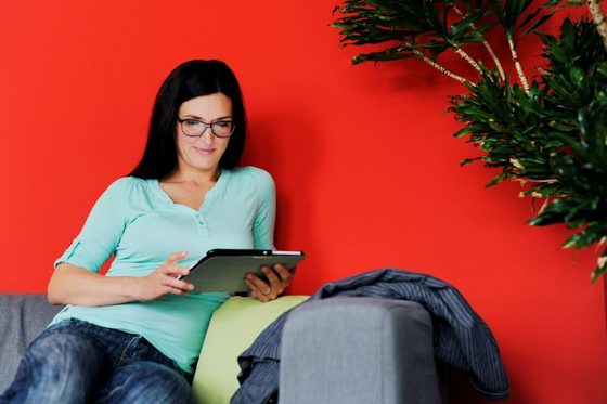 Eine Frau mit Brille lsitzt auf einem Sofa und blickt auf ein Tablet.