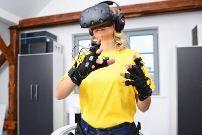 Eine Frau trägt eine Virtual-Reality-Brille und Fingerhandschuhen mit Sensoren.